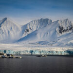 snow-covered-mountain-range-with-a-glacier-and-calm-arctic-ocean-with-several-kittiwake-birds