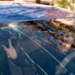 shockedwomanincarwithbrokenwindshieldandcracks-car